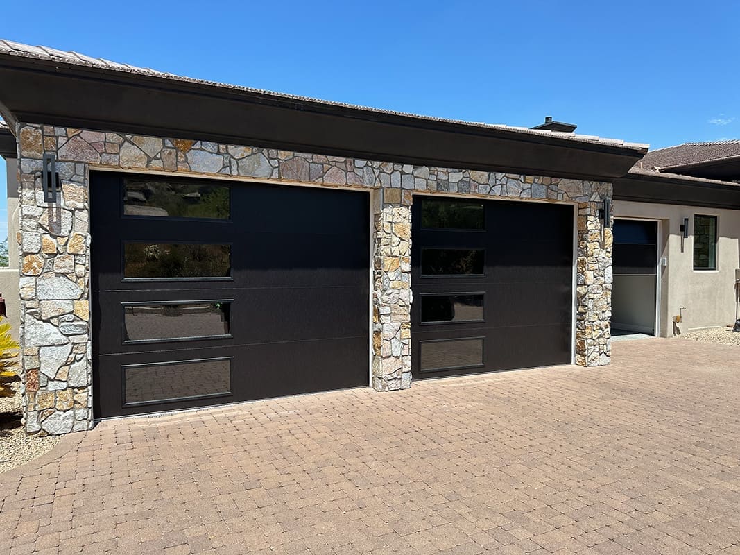 Modern black garage doors with stone accents.